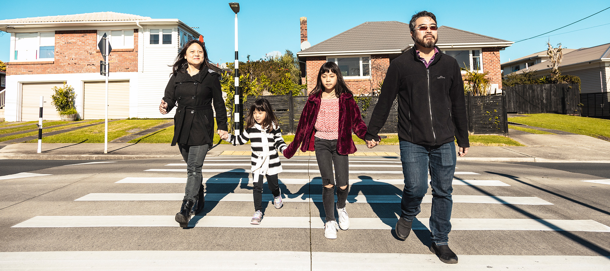 A family of four hold hands and walk across a pedestrian crossing.